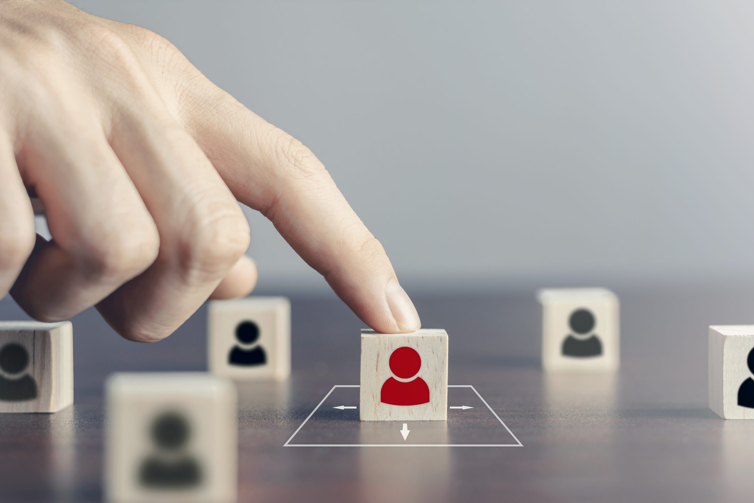 Hand selecting a red figure from wooden blocks, representing personalized and strategic recruitment for the right talent fit.