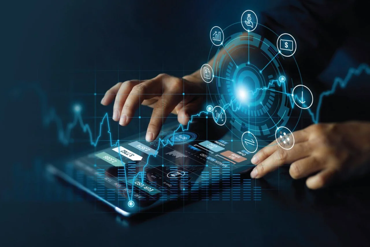 Hands interacting with a tablet displaying a digital interface with analytics, charts, and futuristic icons, symbolizing active monitoring and data visualization.