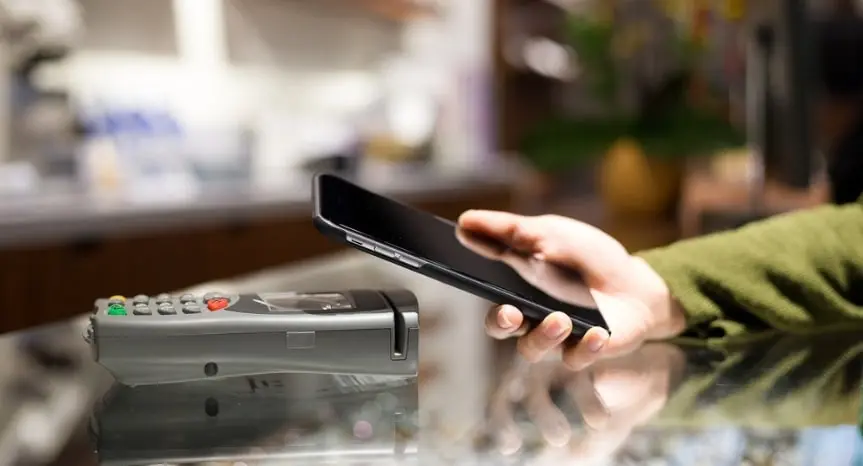 A person using a smartphone to make a contactless payment through a digital point-of-sale terminal, highlighting modern payment solutions.